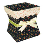 A decorative gift box with a dark navy floral print, a cream scalloped inner liner, a light green ribbon band, and a cream satin bow, shown on a plain white background.