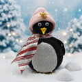 Penguin wearing a pink hat and striped scarf in a snowy scene with snowflakes.