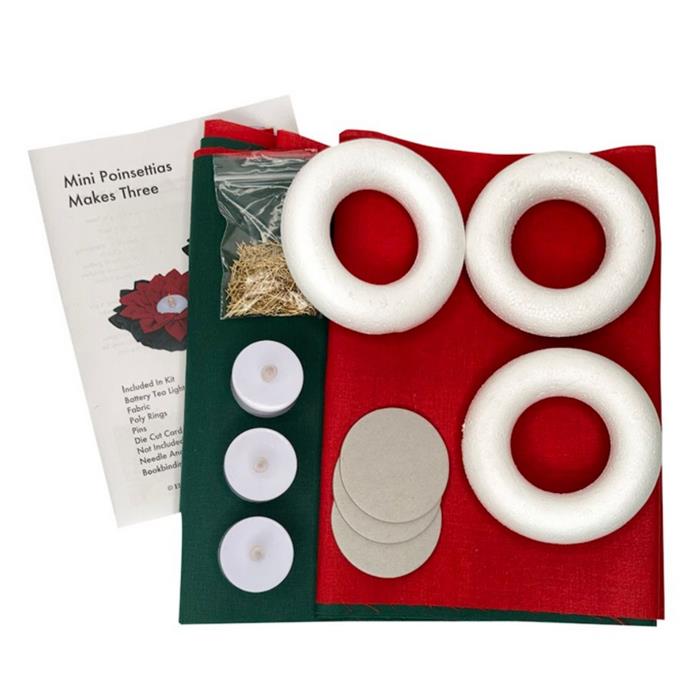 A DIY poinsettia craft kit laid out on a white background, including four white styrofoam wreath forms, a red felt sheet, a dark green felt sheet, round silver metal discs, three white tea light candles, a small bag of dried grass, and an instruction booklet.